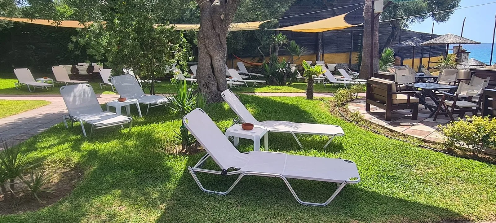 White sunbeds on the grass under shade sails in Kudu's garden, sea in the distance