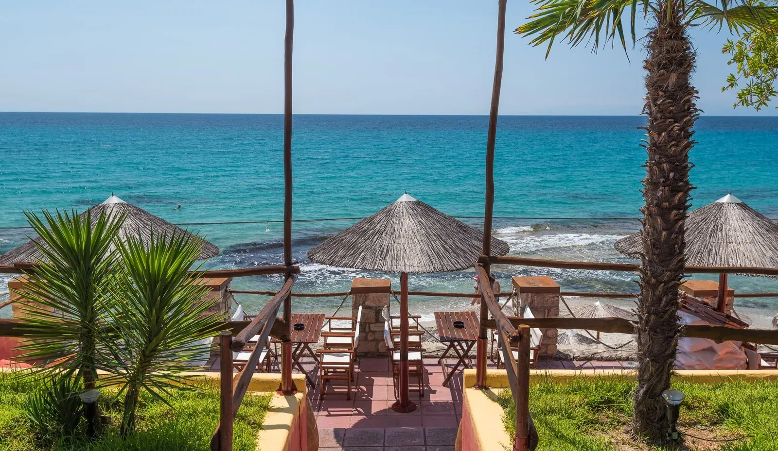 Straw umbrellas on Kudu's terrace above turquoise Aegean water